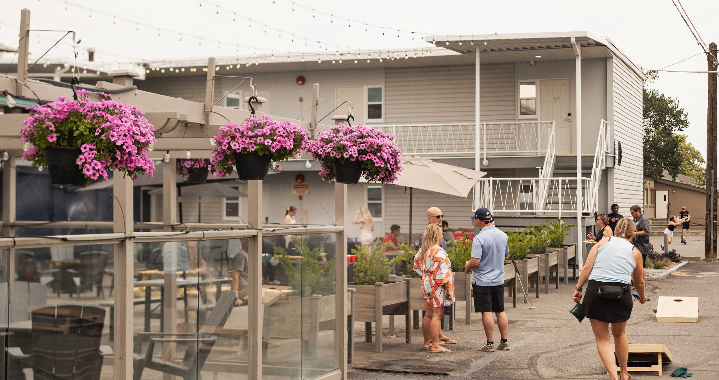 The courtyard is bustling at Scott's Inn, with people playing a beanbag toss, pink flowers hanging from the patio, and people out and about chatting.