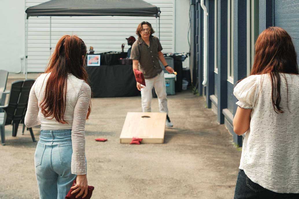 A group of three people are playing cornhole in the courtyard at Scott's Inn.