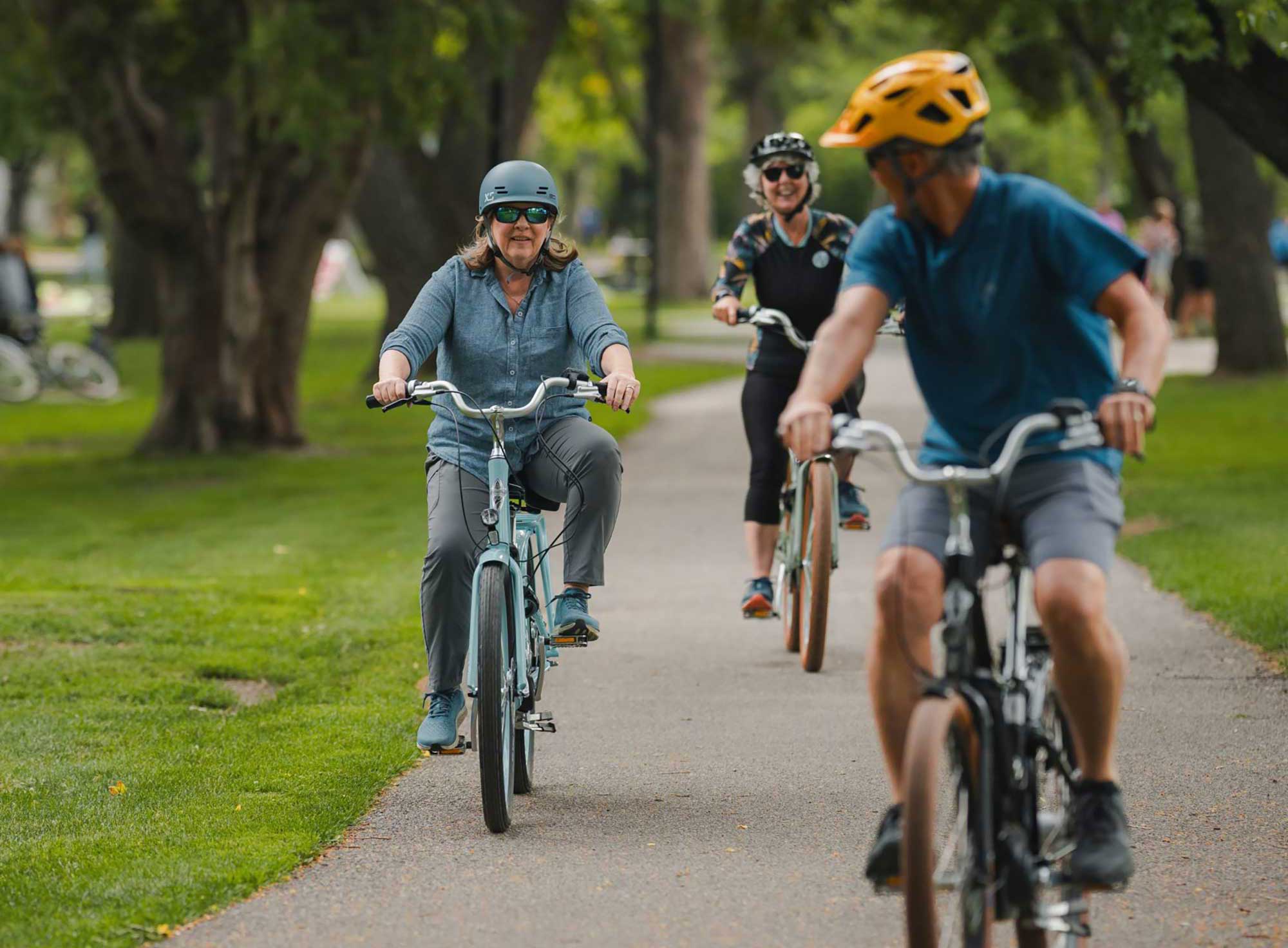 Three seniors are riding bikes together on a shared pathway in a park.
